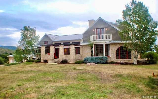 view of front of house with a balcony, stone siding, metal roof, and a front lawn