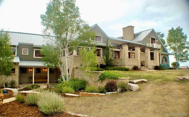 rear view of property with a yard, stone siding, metal roof, and a chimney