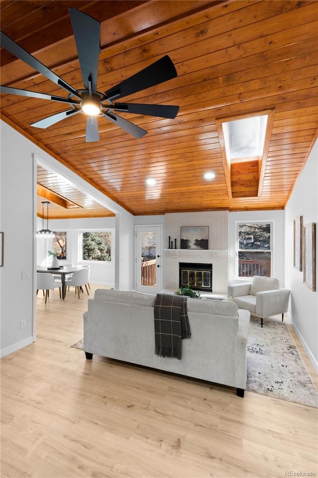 living room with a brick fireplace, light hardwood / wood-style flooring, ceiling fan, a skylight, and wood ceiling