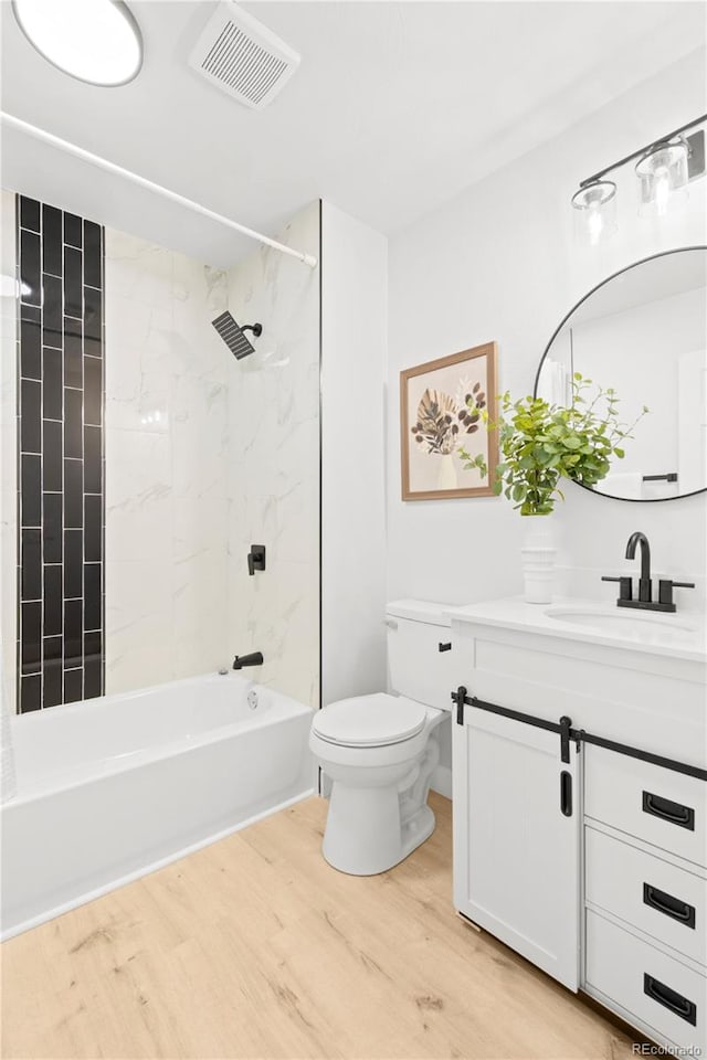 full bathroom featuring hardwood / wood-style floors, vanity, tiled shower / bath combo, and toilet