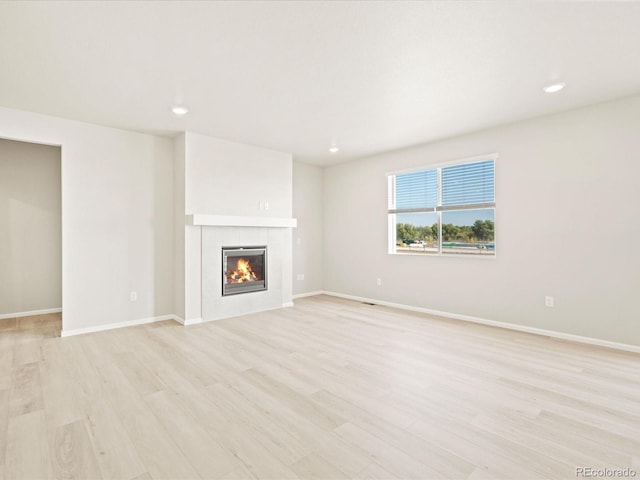 unfurnished living room featuring recessed lighting, a tile fireplace, light wood finished floors, and baseboards