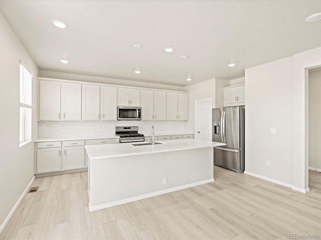 kitchen with a sink, light wood-style floors, light countertops, white cabinets, and appliances with stainless steel finishes