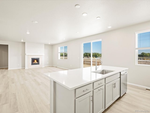 kitchen featuring a sink, an island with sink, dishwasher, light wood finished floors, and light countertops