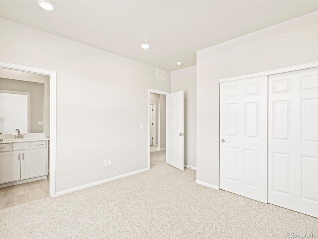 unfurnished bedroom featuring a sink, ensuite bathroom, light colored carpet, baseboards, and visible vents