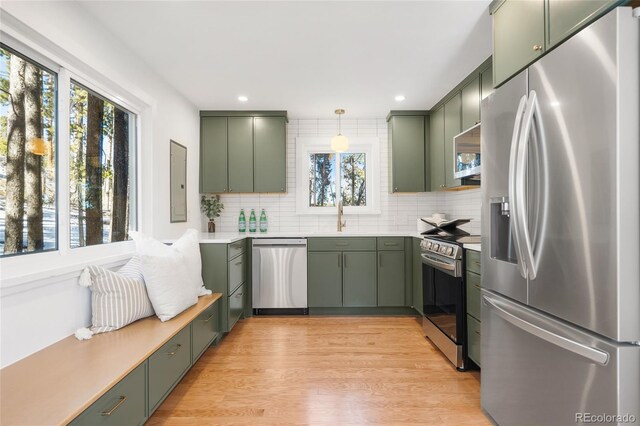 kitchen with appliances with stainless steel finishes, tasteful backsplash, hanging light fixtures, green cabinets, and light hardwood / wood-style flooring