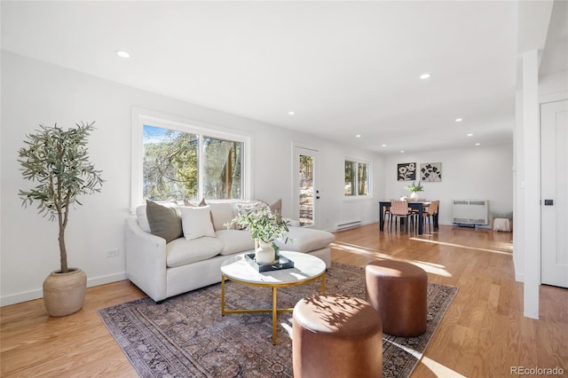 living room with heating unit, a baseboard heating unit, and light hardwood / wood-style floors