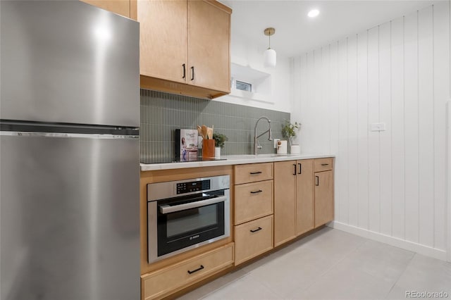 kitchen featuring decorative light fixtures, stainless steel appliances, light brown cabinetry, sink, and light tile patterned flooring