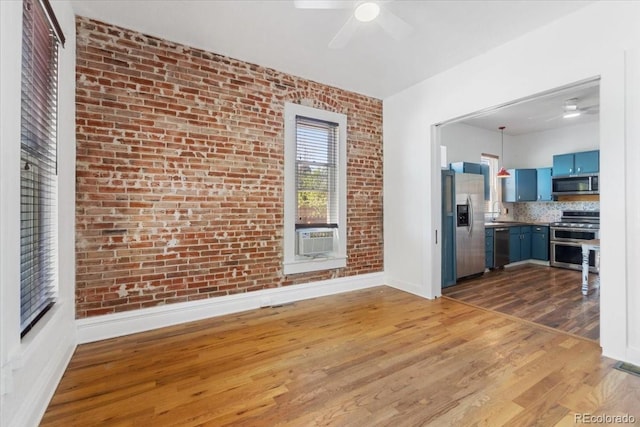 unfurnished living room featuring light wood-style flooring, ceiling fan, a sink, cooling unit, and brick wall