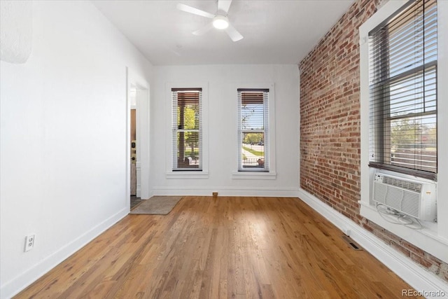 empty room featuring baseboards, wood finished floors, ceiling fan, cooling unit, and brick wall