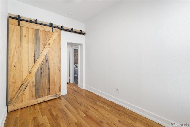 spare room featuring a barn door, baseboards, and wood finished floors