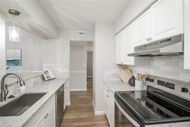 3855 S Monaco St Unit 208, Denver, CO 80237 - kitchen featuring appliances with stainless steel finishes, under cabinet range hood, light wood-style floors, decorative backsplash, and white cabinets