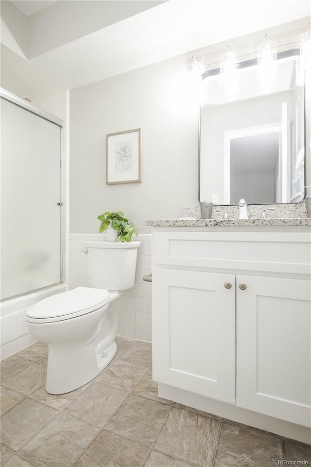 3855 S Monaco St Unit 208, Denver, CO 80237 - bathroom featuring vanity, tile walls, a wainscoted wall, and bath / shower combo with glass door