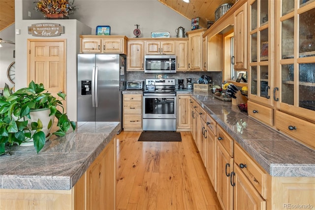 kitchen featuring lofted ceiling, light brown cabinetry, light wood-type flooring, stainless steel appliances, and backsplash