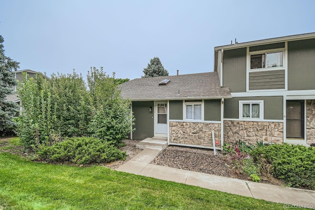 view of front facade with stone siding, a front lawn, and roof with shingles