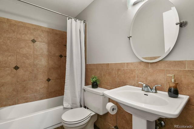 full bathroom with tile walls, toilet, a wainscoted wall, shower / tub combo with curtain, and a sink