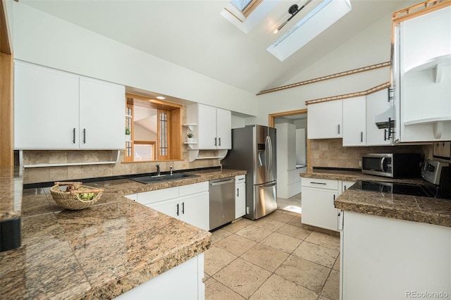 kitchen featuring a skylight, appliances with stainless steel finishes, a sink, open shelves, and backsplash