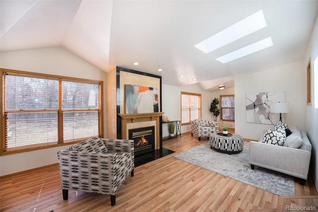 living room featuring lofted ceiling with skylight, a fireplace with flush hearth, and wood finished floors