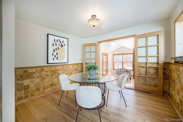 dining room featuring a wainscoted wall, light wood-style flooring, and tile walls