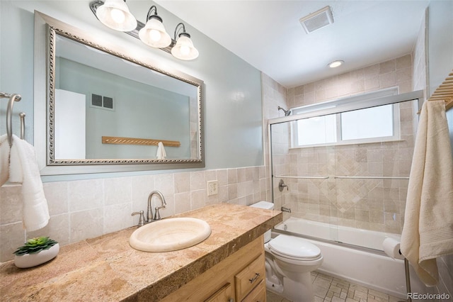 bathroom with toilet, enclosed tub / shower combo, visible vents, and tile walls