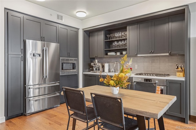 1750 Wewatta St Unit 525, Denver, CO 80202 - kitchen featuring appliances with stainless steel finishes, light countertops, decorative backsplash, open shelves, and light wood-type flooring