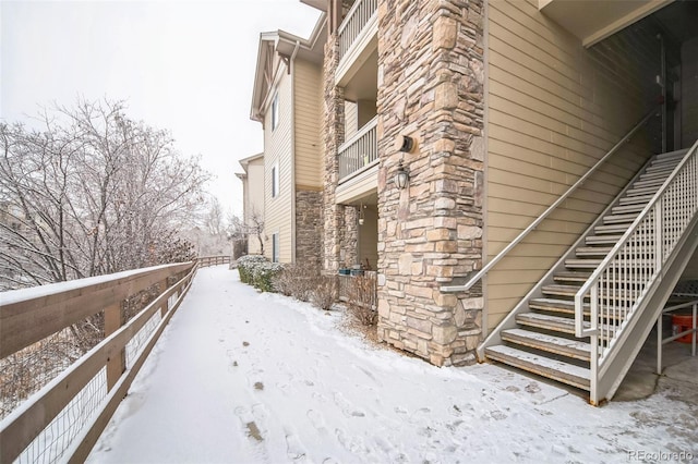 snow covered property featuring stone siding and stairway