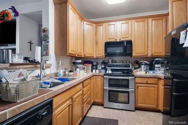 kitchen with light tile patterned floors, black appliances, a sink, and light countertops