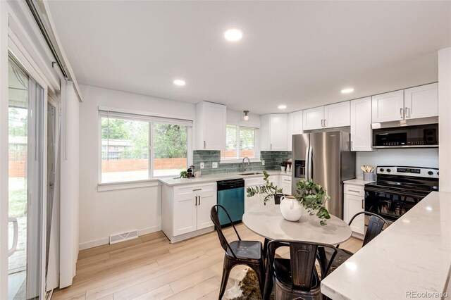 5780 W 5th Ave, Lakewood, CO 80226 - kitchen featuring appliances with stainless steel finishes, white cabinets, light stone counters, light wood-style floors, and decorative backsplash