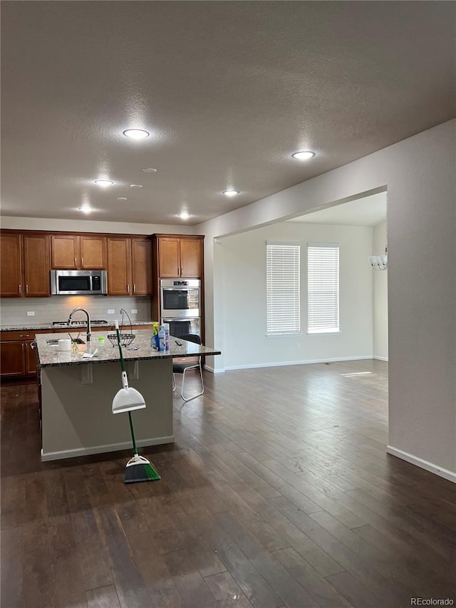 kitchen with a breakfast bar, light stone counters, a center island with sink, appliances with stainless steel finishes, and dark hardwood / wood-style flooring