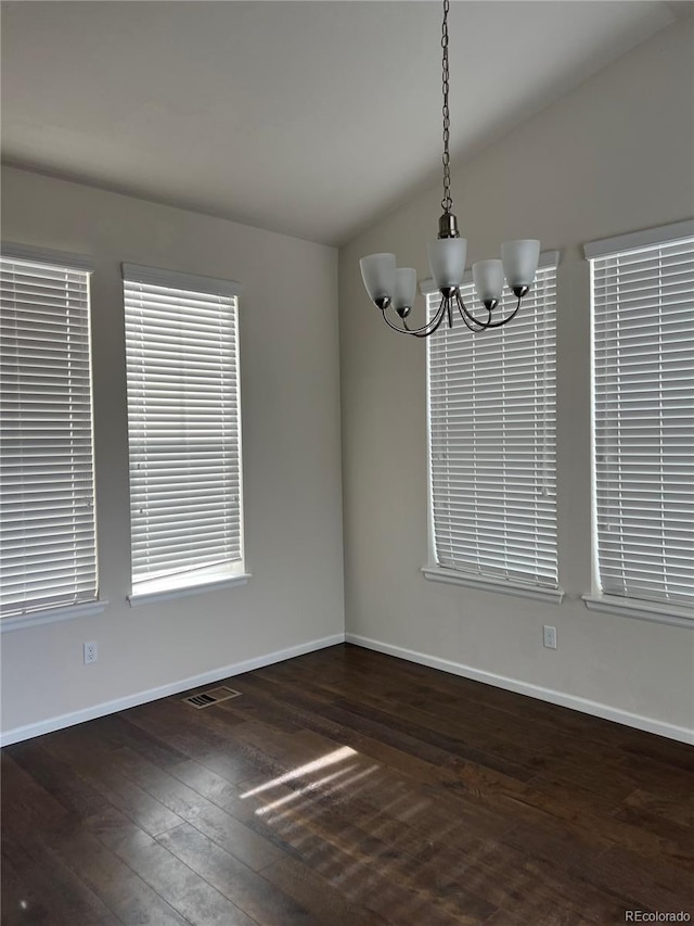 unfurnished dining area featuring lofted ceiling, dark wood-type flooring, a chandelier, and plenty of natural light