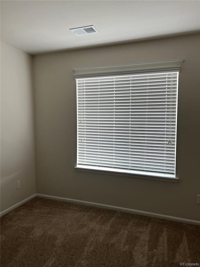 spare room featuring a wealth of natural light and dark colored carpet