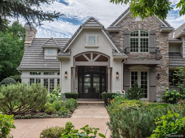 view of front facade featuring stone siding, french doors, a chimney, and stucco siding