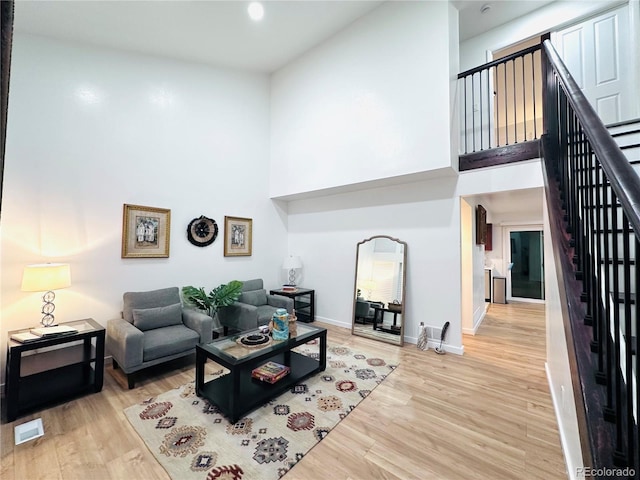 living room with stairway, visible vents, baseboards, light wood-style floors, and a towering ceiling