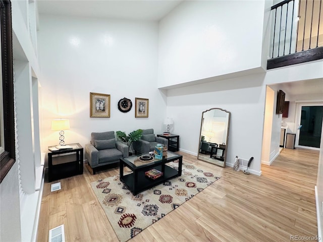 living room with a high ceiling, light wood-style flooring, baseboards, and visible vents