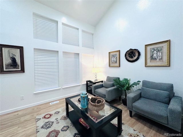 living area with baseboards, wood finished floors, visible vents, and high vaulted ceiling