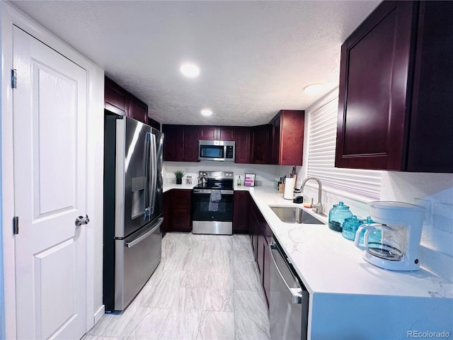 kitchen featuring a sink, a textured ceiling, recessed lighting, stainless steel appliances, and reddish brown cabinets