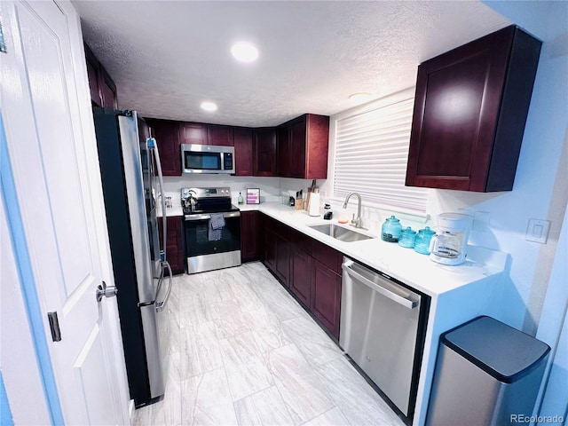 kitchen with a textured ceiling, light countertops, appliances with stainless steel finishes, and a sink