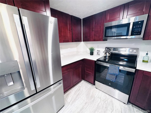 kitchen with light countertops, stainless steel appliances, marble finish floor, a textured ceiling, and reddish brown cabinets