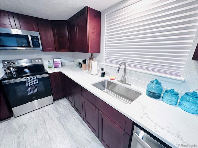 kitchen with reddish brown cabinets, light stone countertops, stainless steel appliances, and a sink