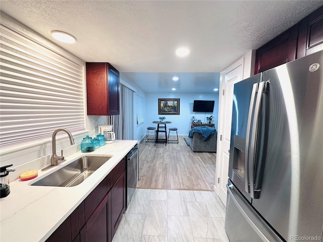 kitchen with a sink, stainless steel appliances, light stone countertops, and a textured ceiling