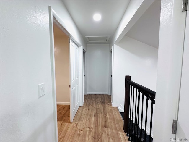 corridor with an upstairs landing, baseboards, attic access, and light wood-style flooring