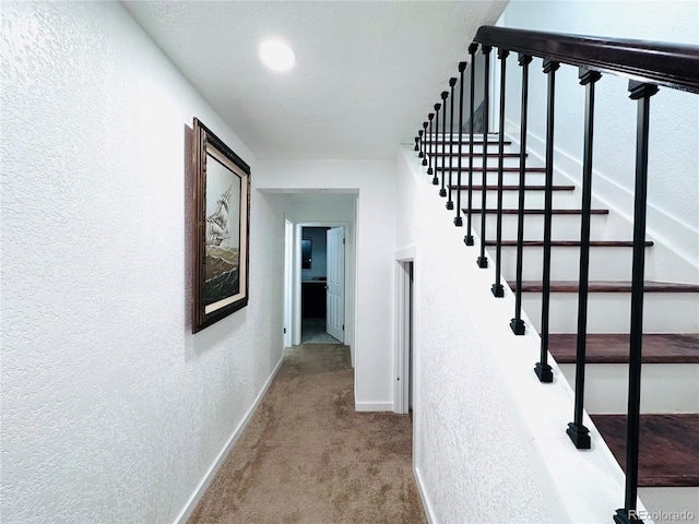 corridor with stairway, carpet flooring, a textured wall, and baseboards