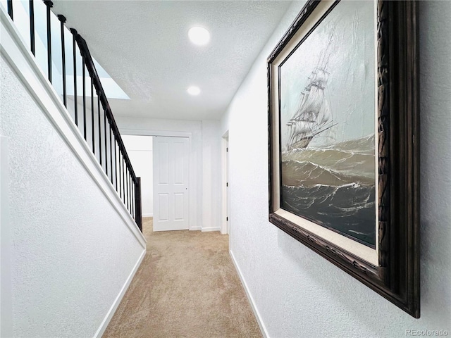 hall featuring stairway, baseboards, a textured ceiling, carpet flooring, and a textured wall