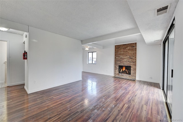 unfurnished living room featuring a ceiling fan, visible vents, dark wood-style flooring, a textured ceiling, and a brick fireplace