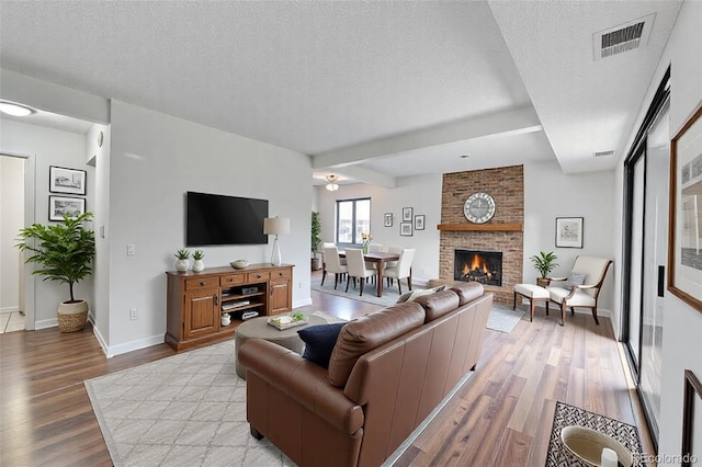 living area featuring visible vents, a textured ceiling, a brick fireplace, and wood finished floors