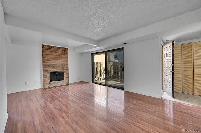 unfurnished living room with a brick fireplace, baseboards, wood-type flooring, and a textured ceiling