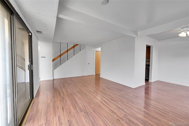 spare room with a ceiling fan, stairs, light wood-style floors, and visible vents