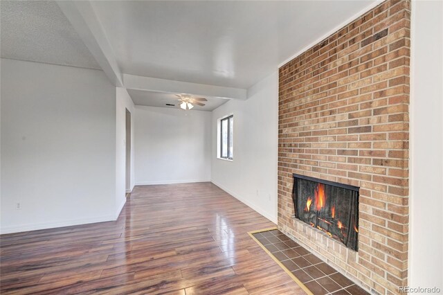 unfurnished living room featuring a ceiling fan, wood finished floors, a fireplace, and baseboards