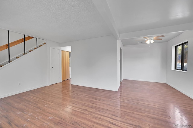 spare room featuring ceiling fan, baseboards, stairway, hardwood / wood-style flooring, and a textured ceiling