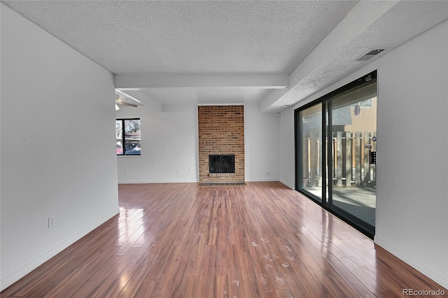 unfurnished living room featuring baseboards, visible vents, a fireplace, hardwood / wood-style flooring, and a textured ceiling