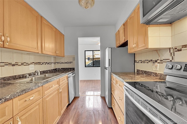 kitchen with a sink, tasteful backsplash, dark countertops, wood finished floors, and appliances with stainless steel finishes